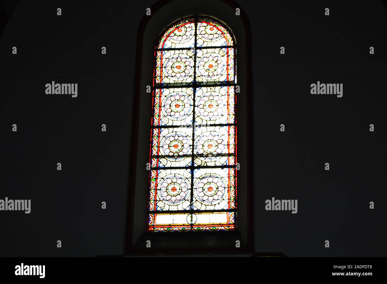 La luce del sole si riversa attraverso il variopinto vetrate della Chiesa contro una parete scura, gli interni della cattedrale cattolica Foto Stock