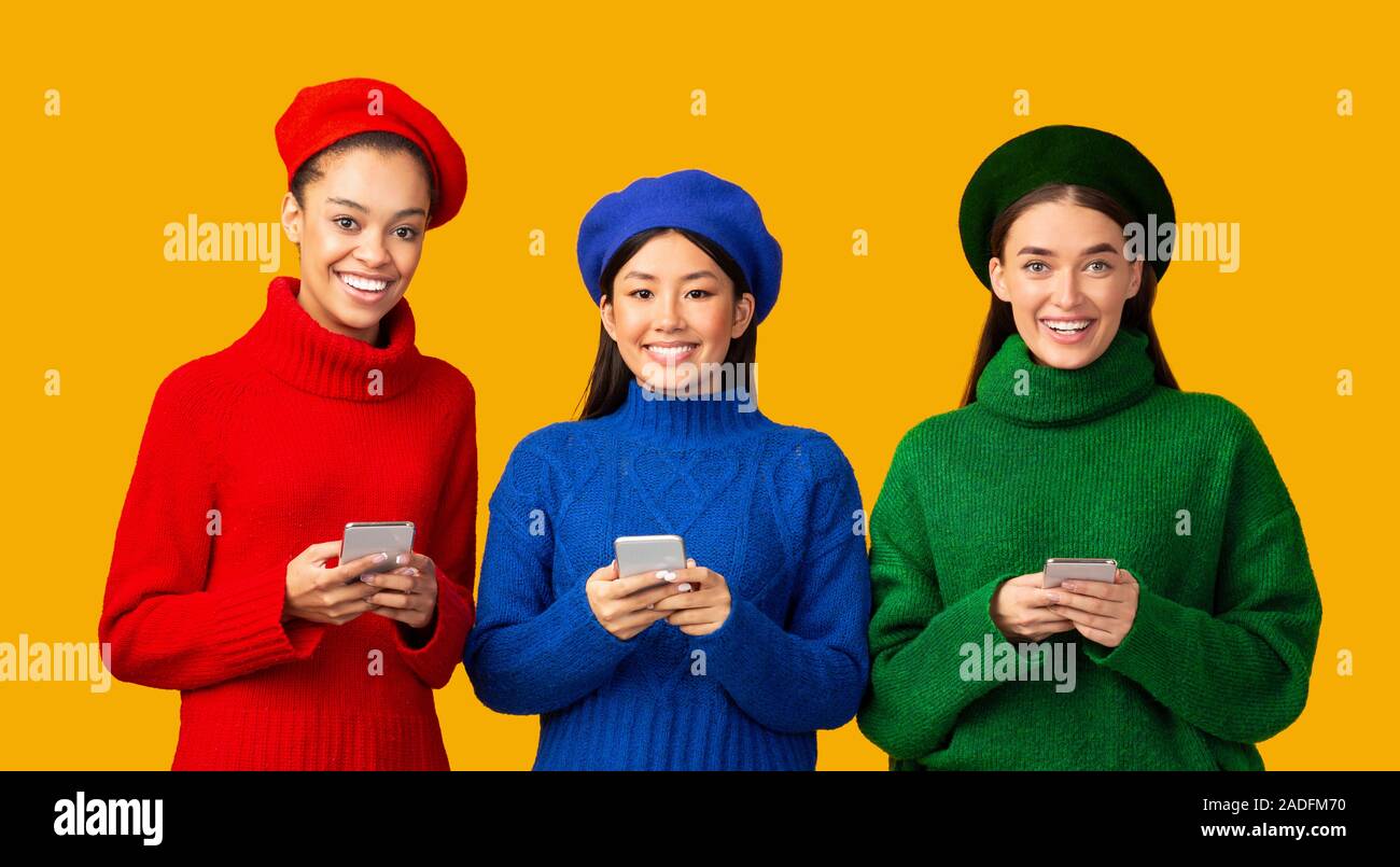 Tre ragazze multietnica utilizzando gli smartphone in piedi su sfondo giallo, Panorama Foto Stock