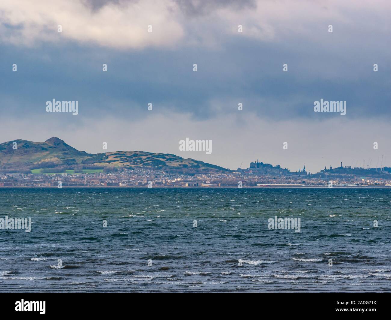 Longniddry Bents, East Lothian, Scozia, Regno Unito, 4 dicembre 2019. Regno Unito: Meteo una oscura minaccia sky si diffonde attraverso la skyline di Edimburgo in una giornata di vento con Arthur' Seat, il Castello di Edimburgo, Calton Hill monumenti e la gru alta del St James riqualificazione lavori di costruzione visibile. Vista da Longniddry Bents attraverso il Firth fo indietro Foto Stock