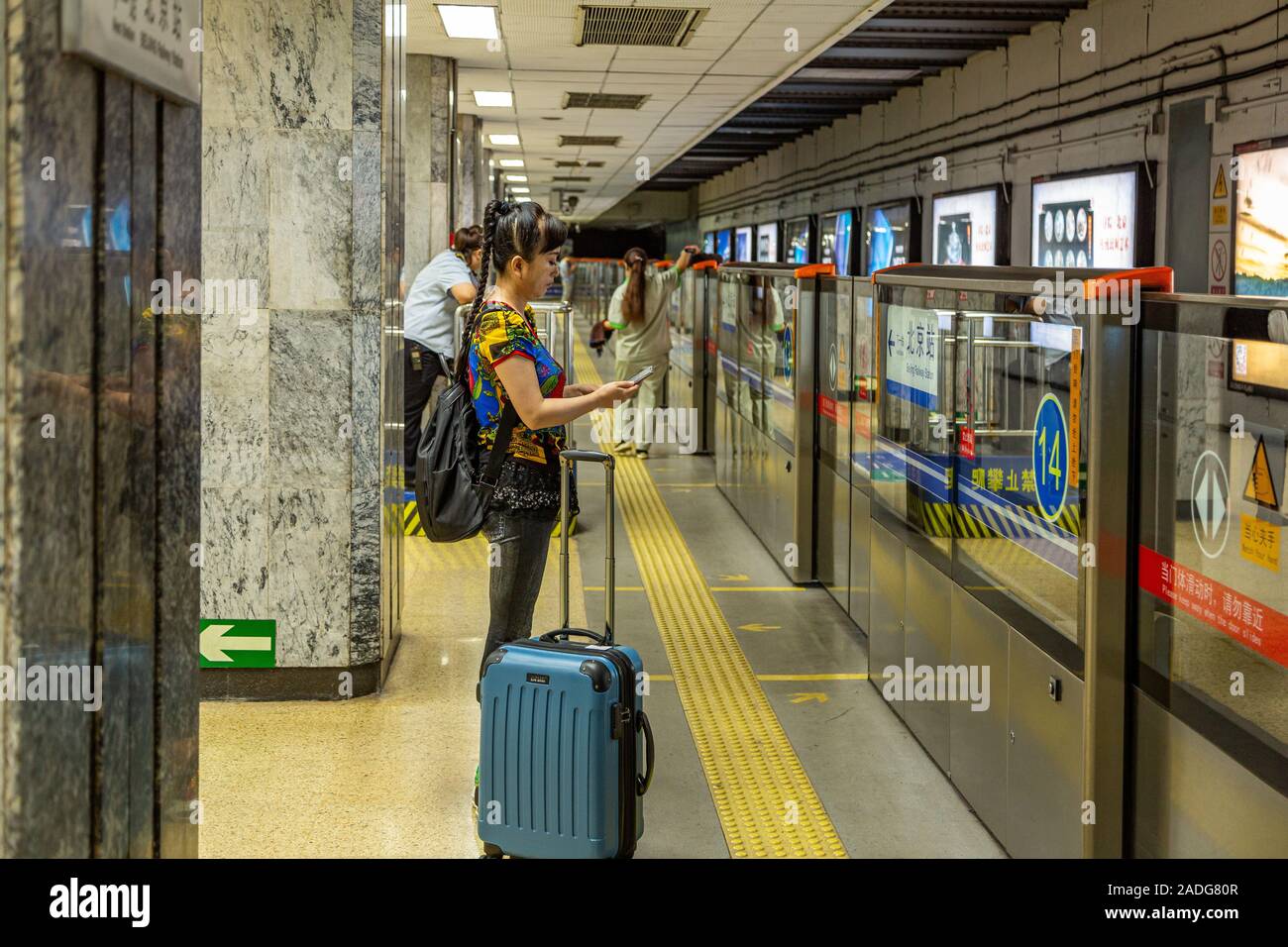 Una donna che guarda un telefono attende il treno alla stazione di Chongwenmen Interchange sulla linea 2 e sulla linea 5 della metropolitana di Pechino, Pechino Cina Foto Stock