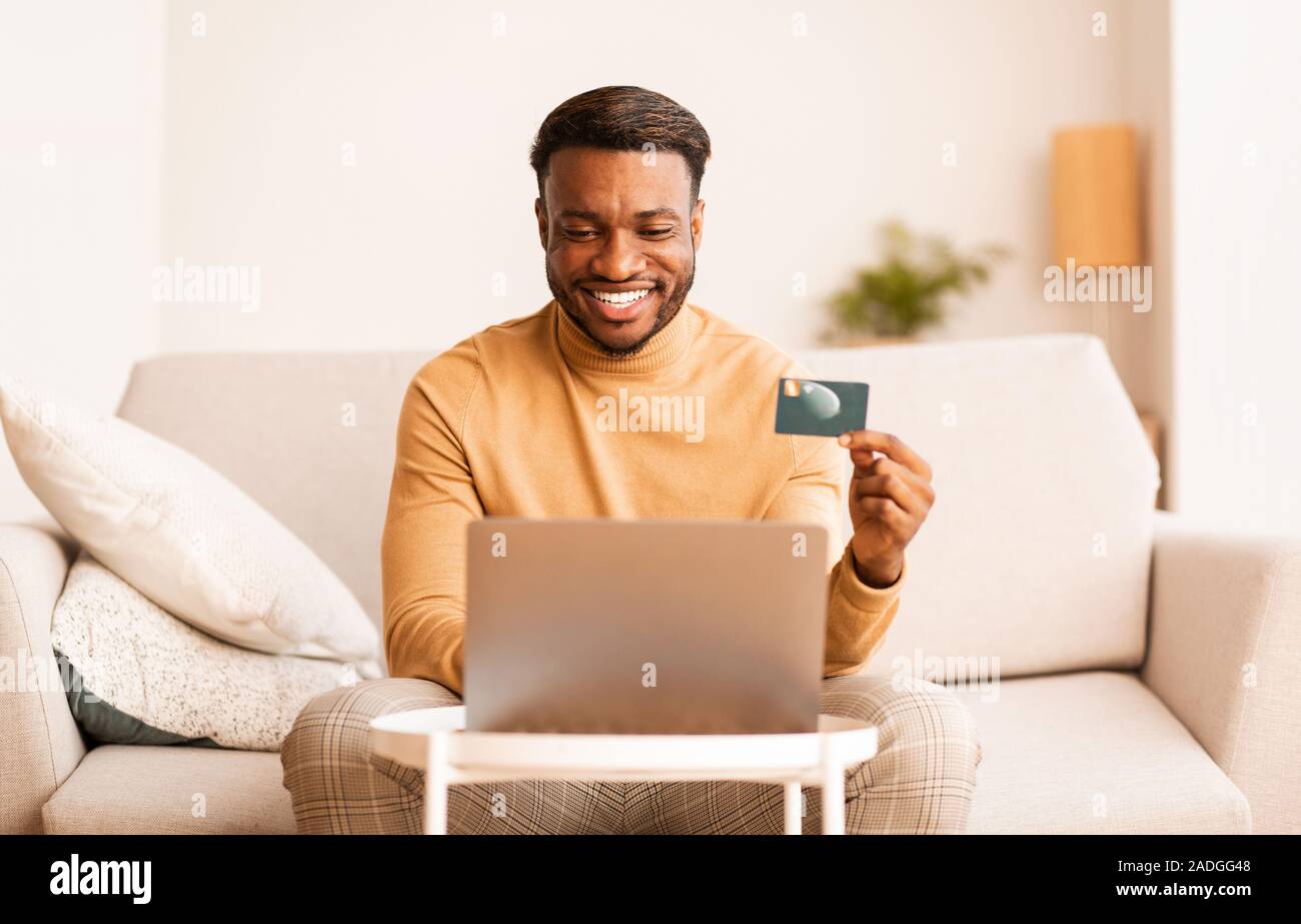 Happy Guy Holding Carta di Credito utilizzando Laptop seduti a casa Foto Stock