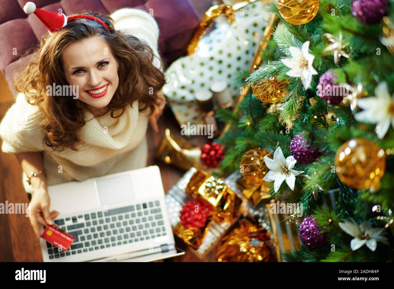 Sorridente casalinga alla moda in oro zecchino gonna e maglione bianco con  carta di credito facendo shopping on line sul sito di e-commerce e sotto  decorate Christm Foto stock - Alamy