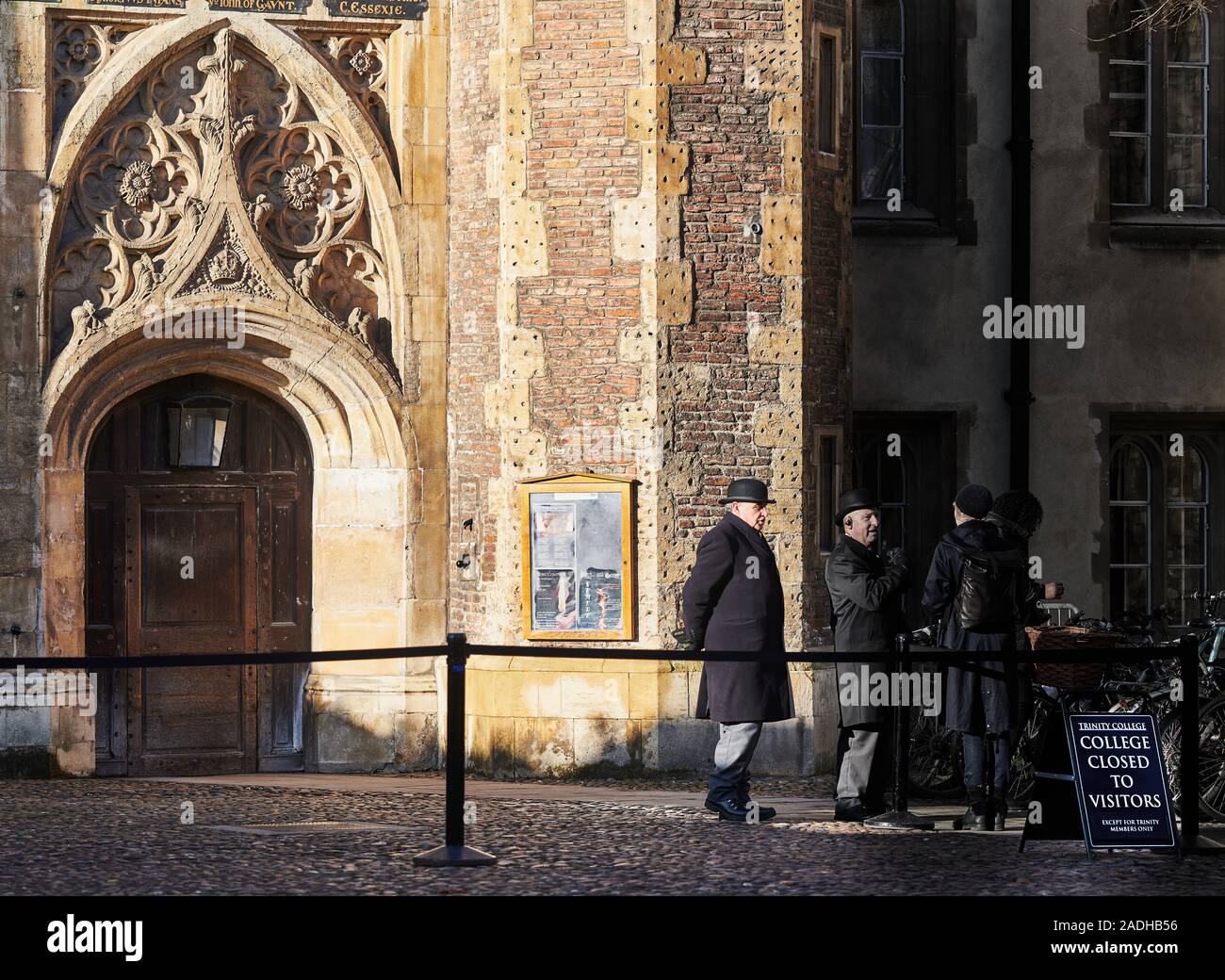 Due guardie di sicurezza in Bowler Hats presso l'ingresso principale al Trinity College di Cambridge University, Inghilterra, su una soleggiata giornata invernale. Foto Stock