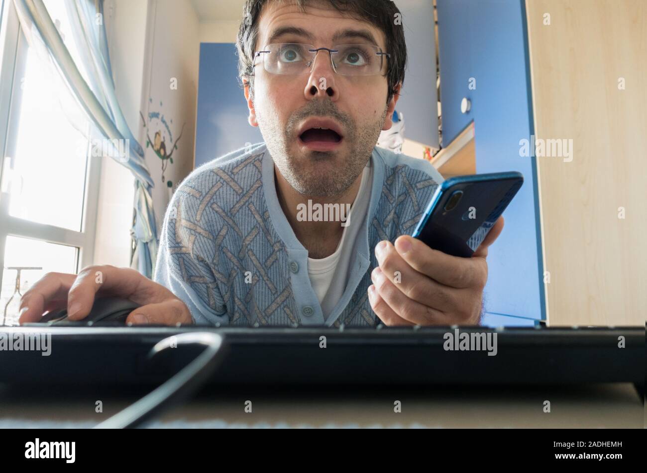Giovane uomo in pigiama addicted a computer e smartphone in camera da letto. Concetto di dipendenza dalle tecnologie e la mancanza di vita sociale Foto Stock