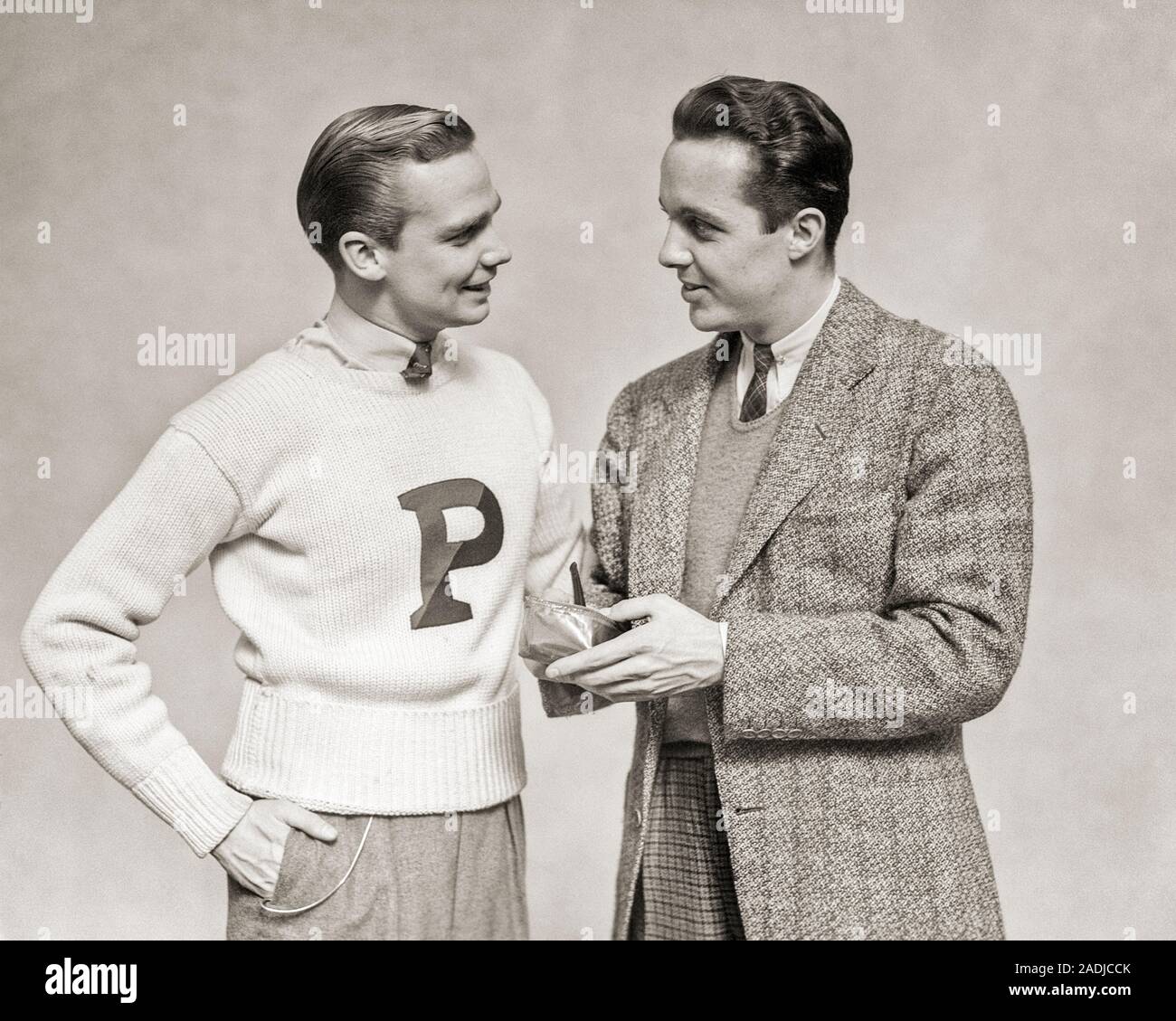 1930 Collegio maschile studente lettera che indossa un maglione parlando di uomo più anziano di indossare tuta e legare il riempimento il suo tubo dalla sacca di tabacco - S3587 HAR001 HARS amicizia a mezza lunghezza persone maschi FRATELLI B&W GUY riempiendo la sua università di tabacco e custodia in occasione di pari livello di istruzione superiore amichevole concettuale reclutamento collegi elegante P CONSULENZA facoltà convivere giovane adulto uomo BIANCO E NERO ETNIA CAUCASICA HAR001 in vecchio stile Foto Stock