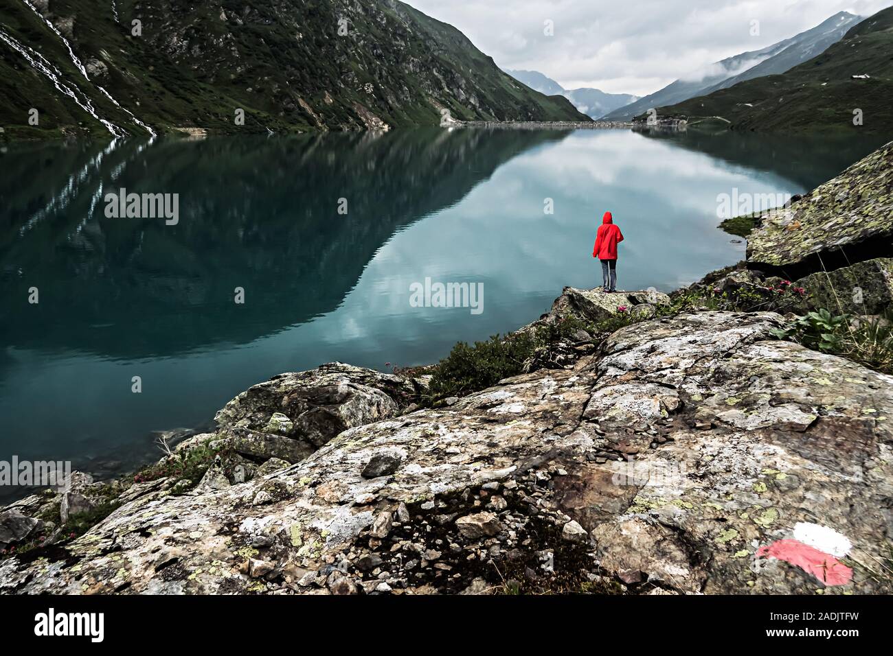Un singolo escursionista in un cappotto rosso permanente al Lago Kartell al di sopra di San Anton a Arlberg in Austria Foto Stock