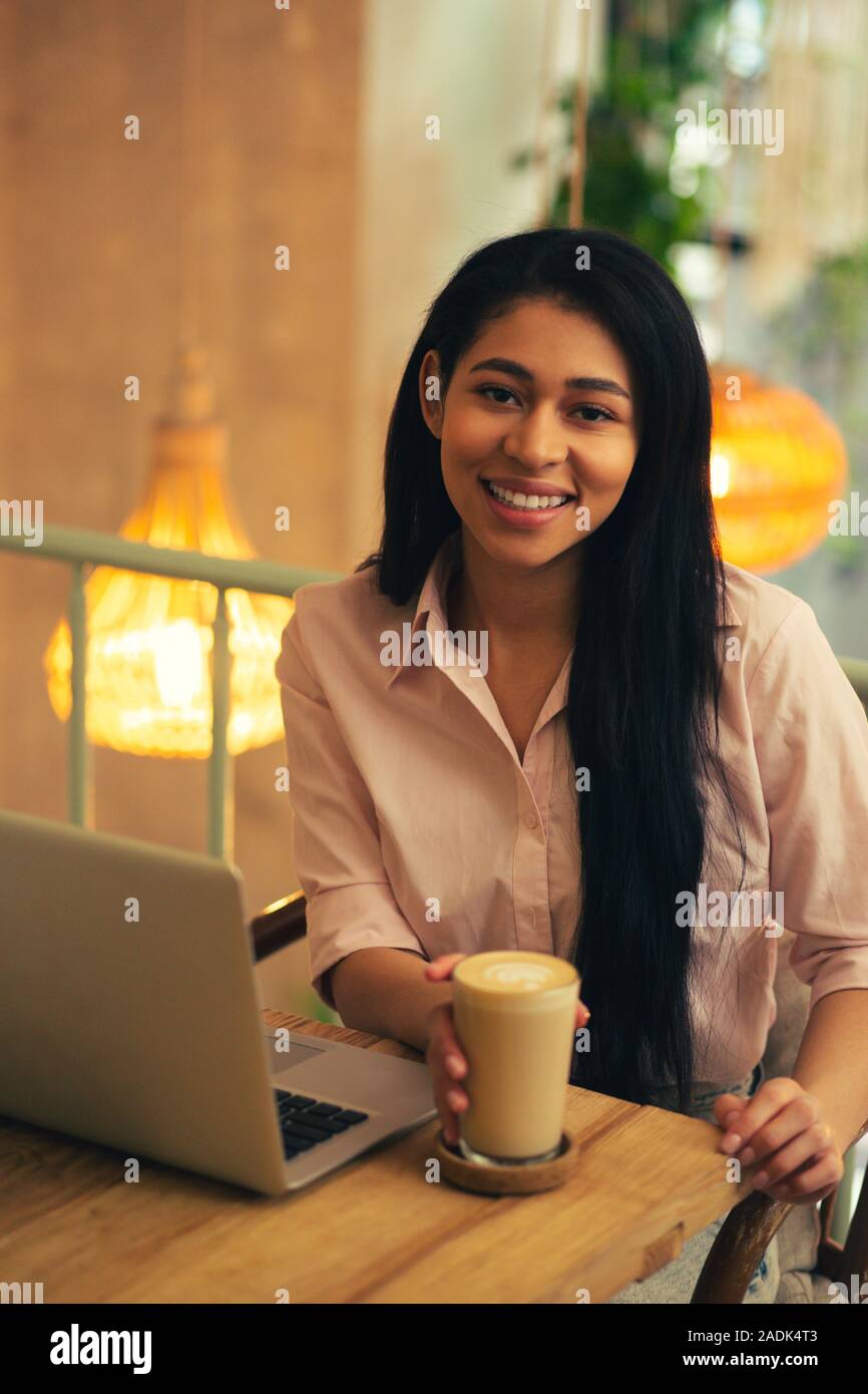 Fiducioso freelancer seduto con il latte nel caffè e sorridente Foto Stock