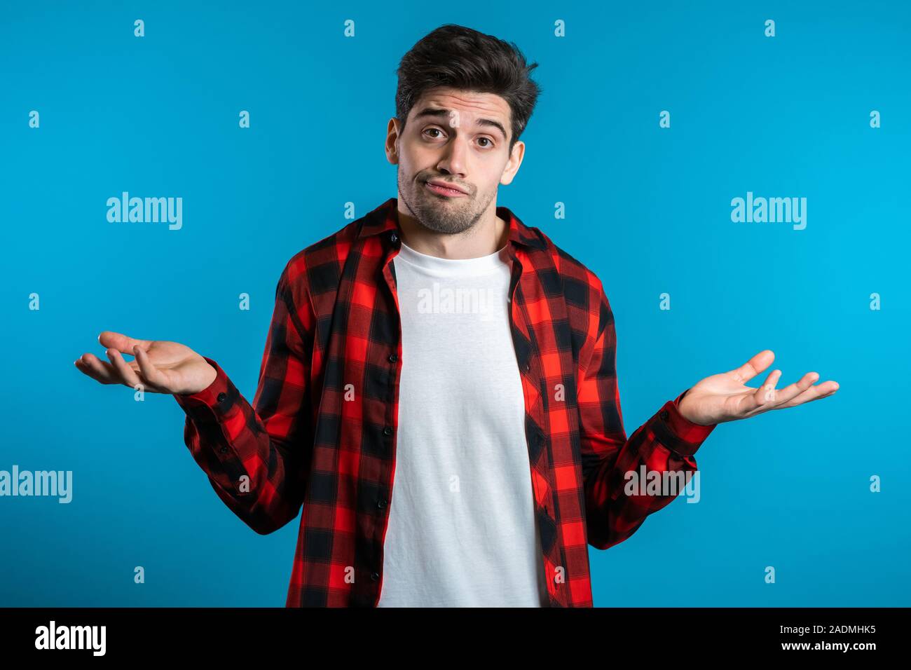 Giovane bello sicuri guy in rosso plaid shirt alza le spalle le sue braccia, Fa gesto di non so, non aiutano a nulla. Foto Stock