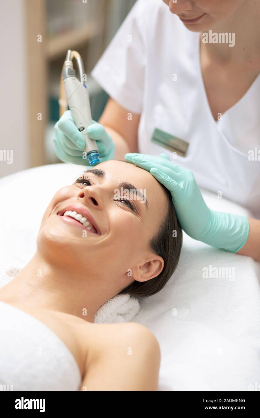 Donna positiva di ridere mentre estetista a nutrire la sua pelle Foto Stock