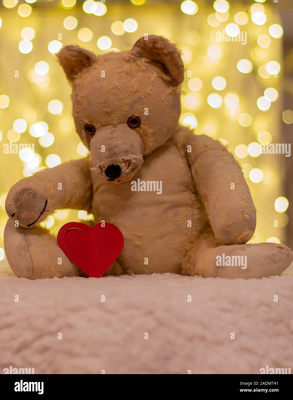 Molto vecchio giocattolo morbido. Tra 40-50 anni orsacchiotto con carta rossa cuore. Sullo sfondo sono le luci di Natale. Nostalgia, amore. Foto Stock