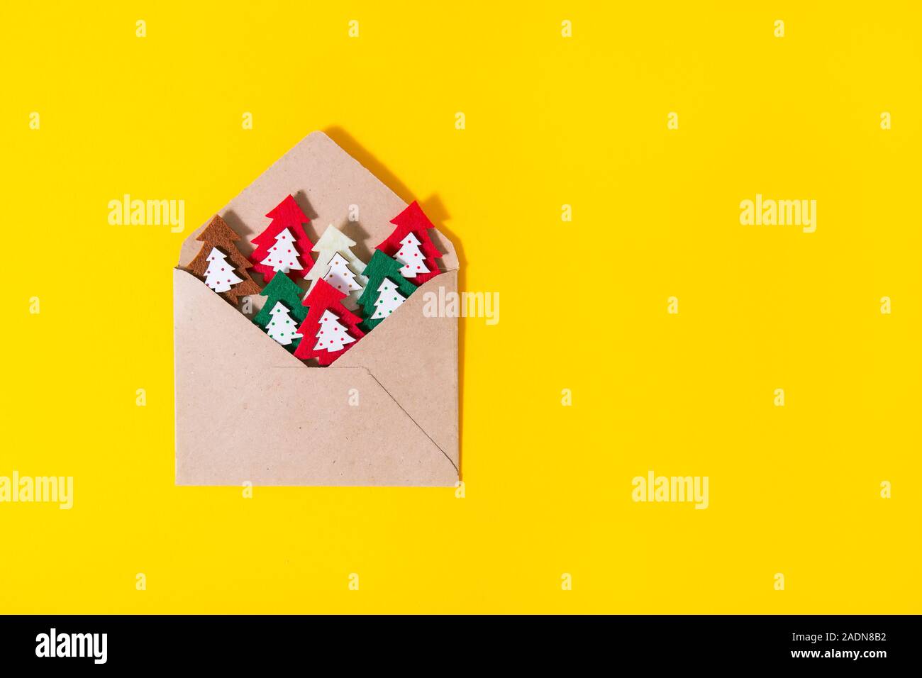 Craft paperenvelope con feltro di alberi di Natale figure luminose su sfondo giallo. Semplice minimalista scheda festosa concetto. Saluti fatti a mano. Appartamento Foto Stock
