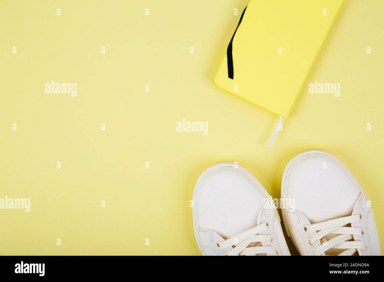 Coppia di sneakers giallo e notebook su sfondo giallo, vista dall'alto Foto Stock