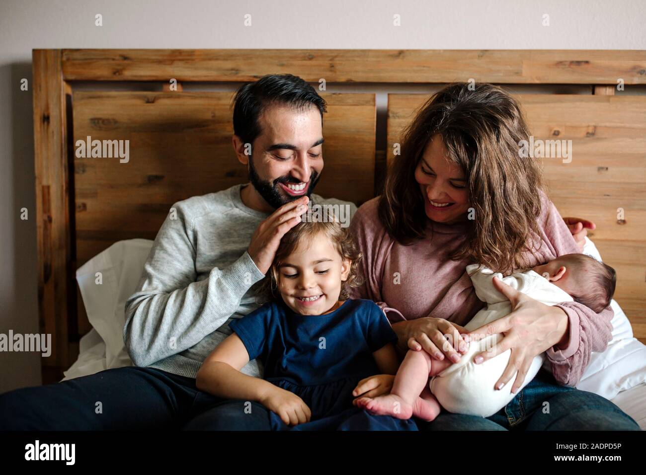 Felice famiglia amorevole coccolati sul letto con neonati e bambina di 4 anni Foto Stock
