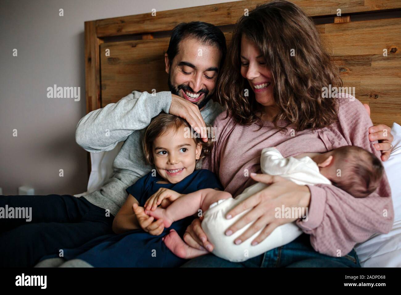 Famiglia sorridente coccolati insieme sul letto come madre breastfeeds neonato Foto Stock