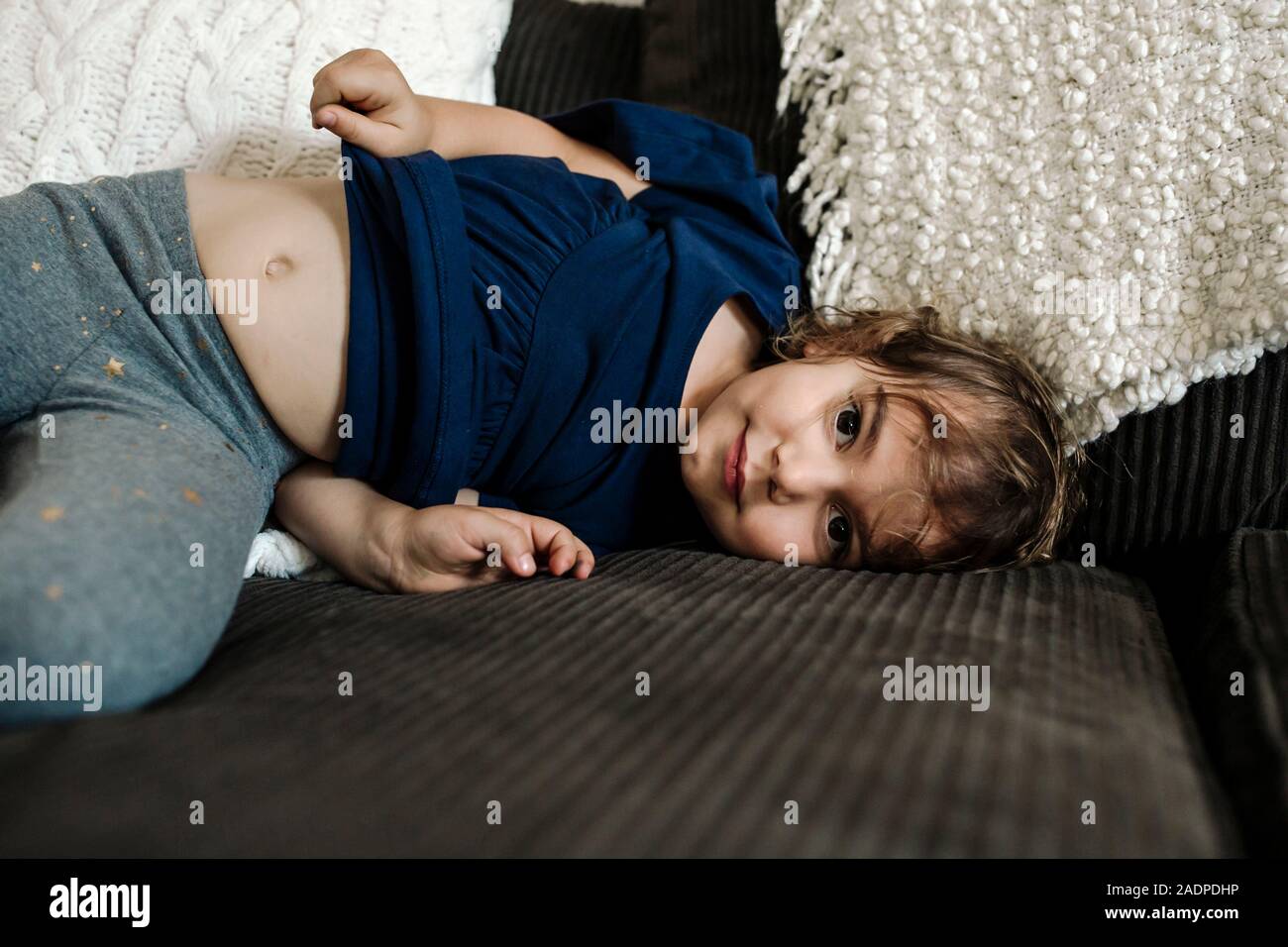 4 yr old girl sdraiato sul divano con la pancia che mostra Foto Stock