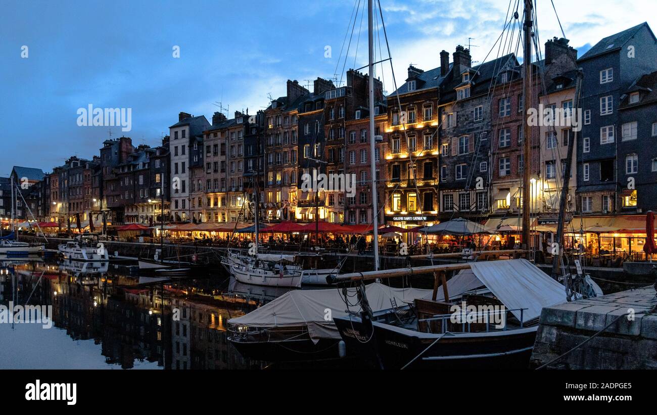 Barche ormeggiate nel vecchio porto di Honfleur, la Francia con le sue terrazze dei caffé al blue ora Foto Stock