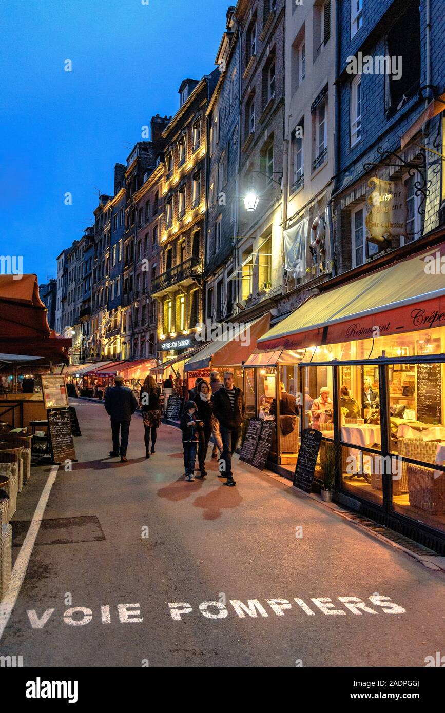 I pedoni a piedi da cafe' sul Quai Sainte-Catherine al vecchio porto di Honfleur, Francia al blue ora Foto Stock