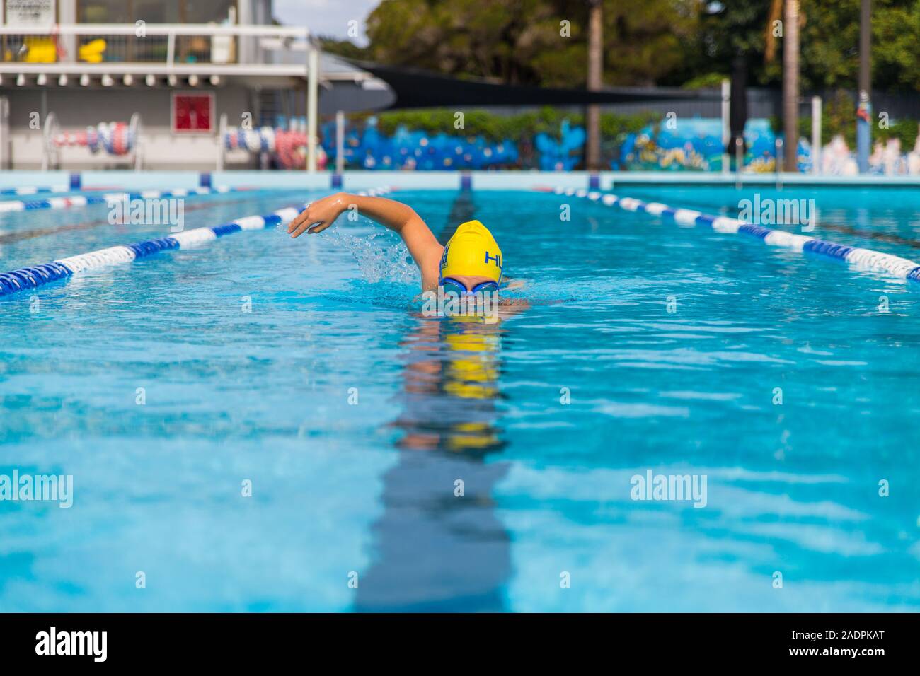 Una donna di nuoto in una piscina pubblica con una nuotata giallo cappello e occhiali facendo il freestyle crawl anteriore corsa nuoto Foto Stock