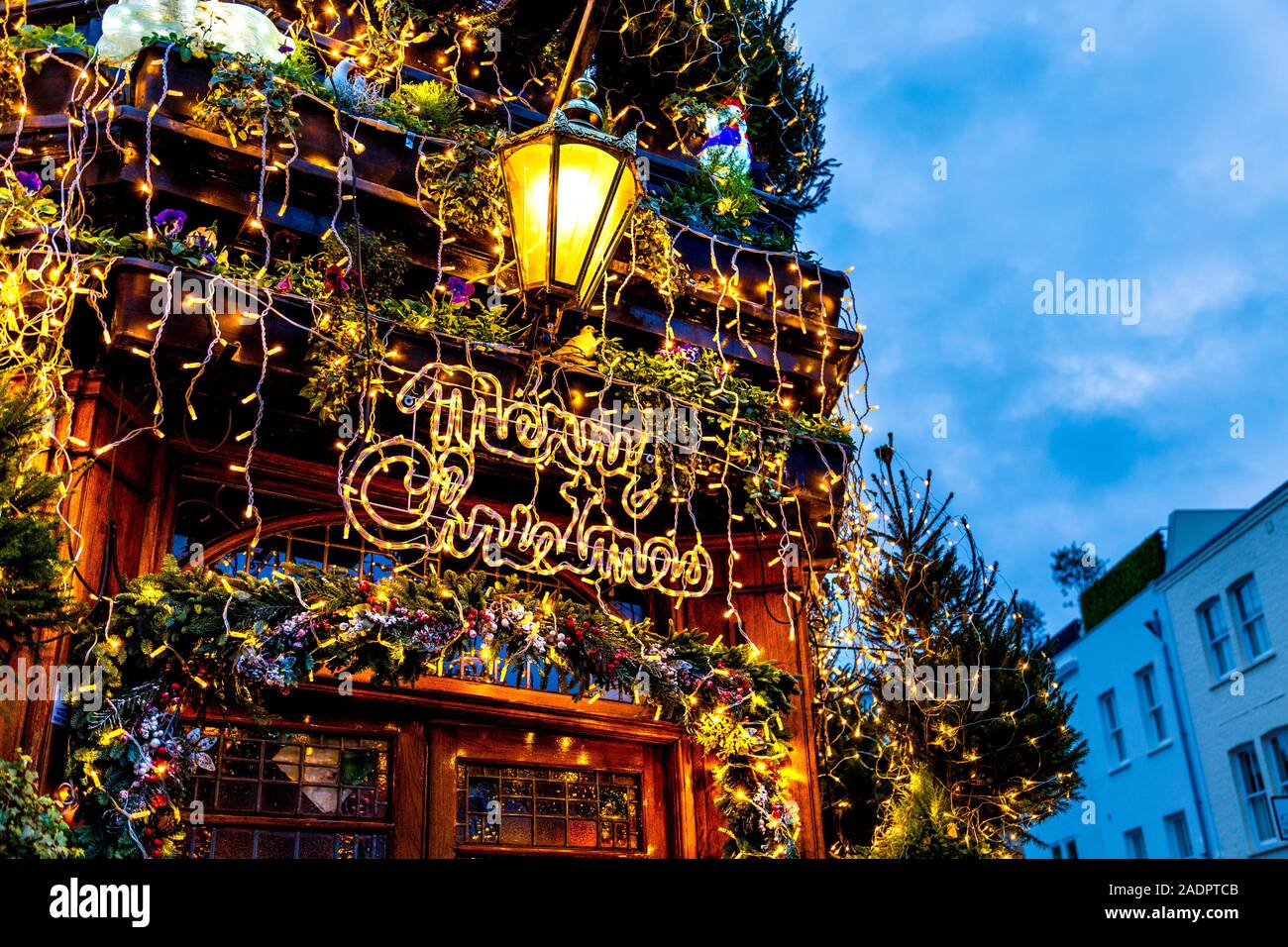 Buon Natale e opulente luci e decorazioni natalizie sulla facciata del Churchill Arms Pub, Londra, Regno Unito Foto Stock