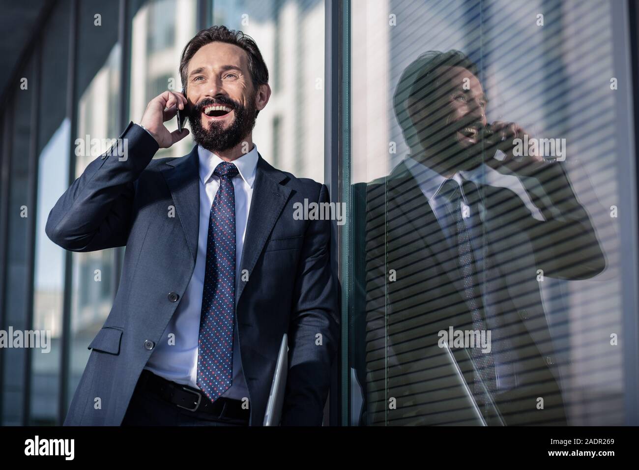 Overjoyed imprenditore sorridente in piedi contro la parete in vetro Foto Stock