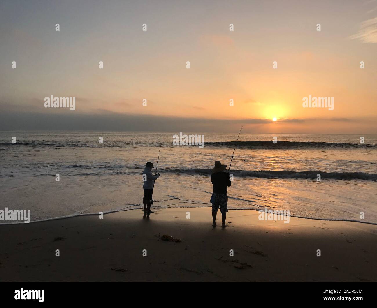 Gli uomini di pesca da surf da una spiaggia in Malibu al tramonto a Los Angeles, CA Foto Stock