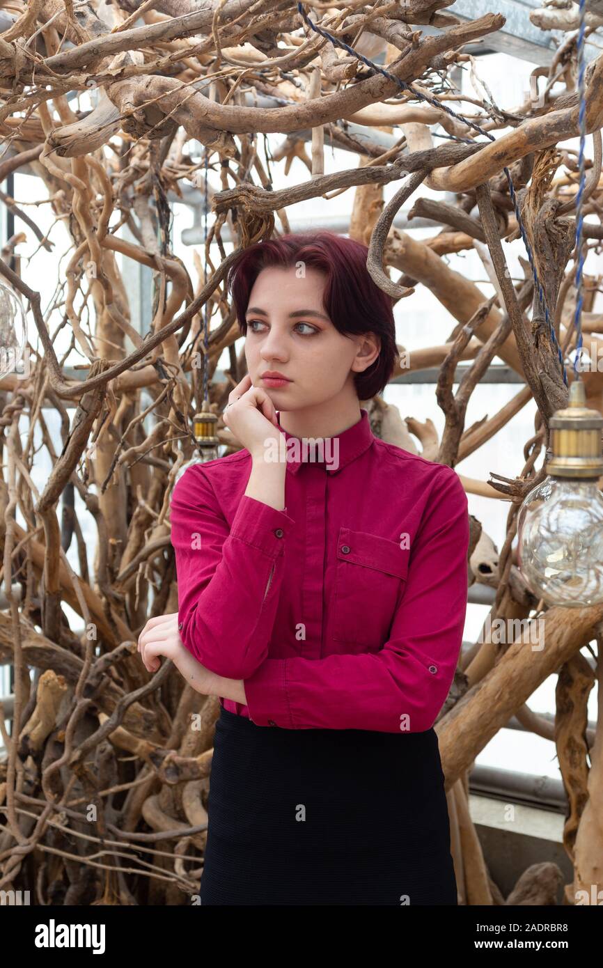 Ragazza in una camicia rossa e mantello contro uno sfondo bianco di alberi Foto Stock