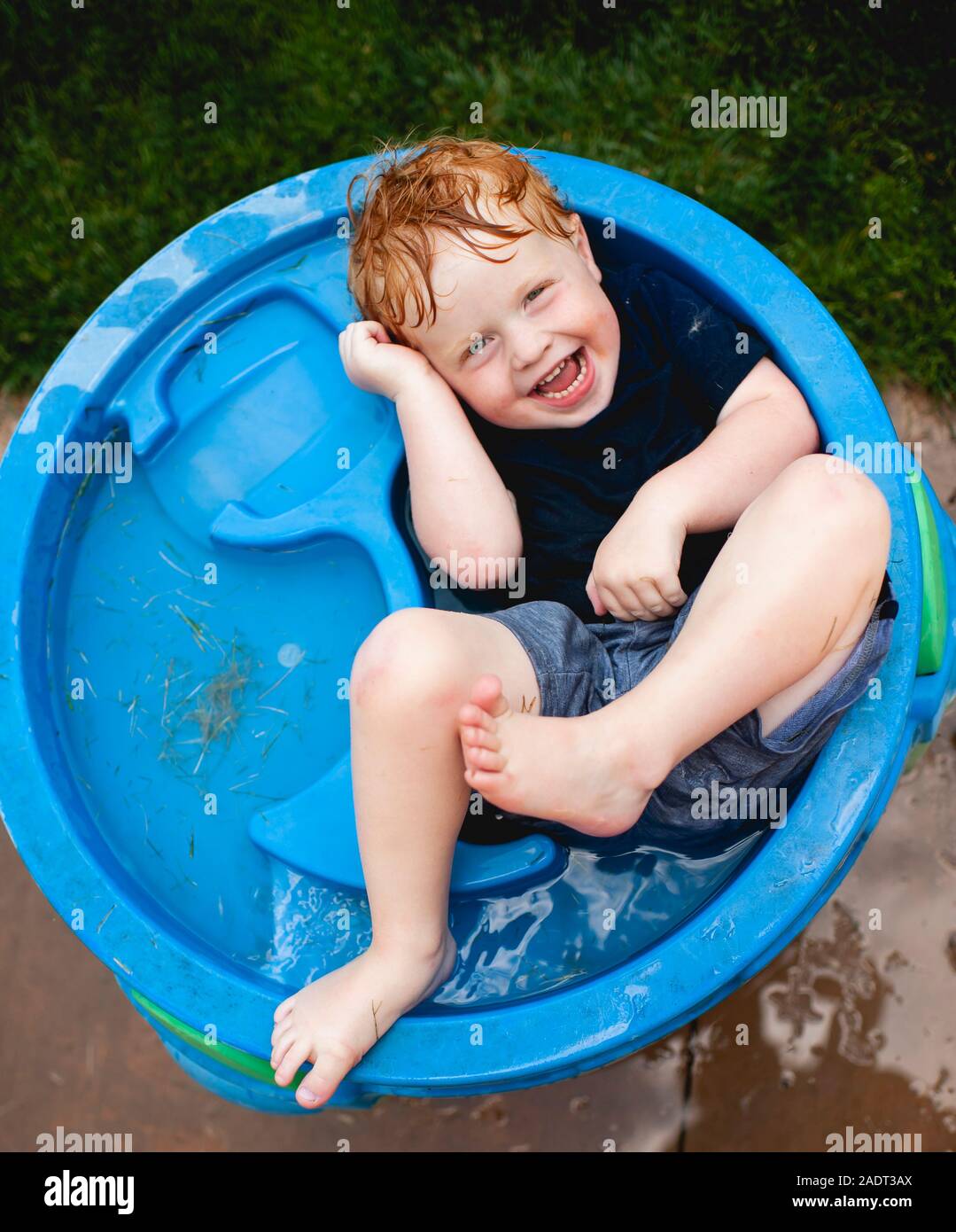Il Toddler boy posa in acqua a tavola con vestiti sul ridere in cortile Foto Stock