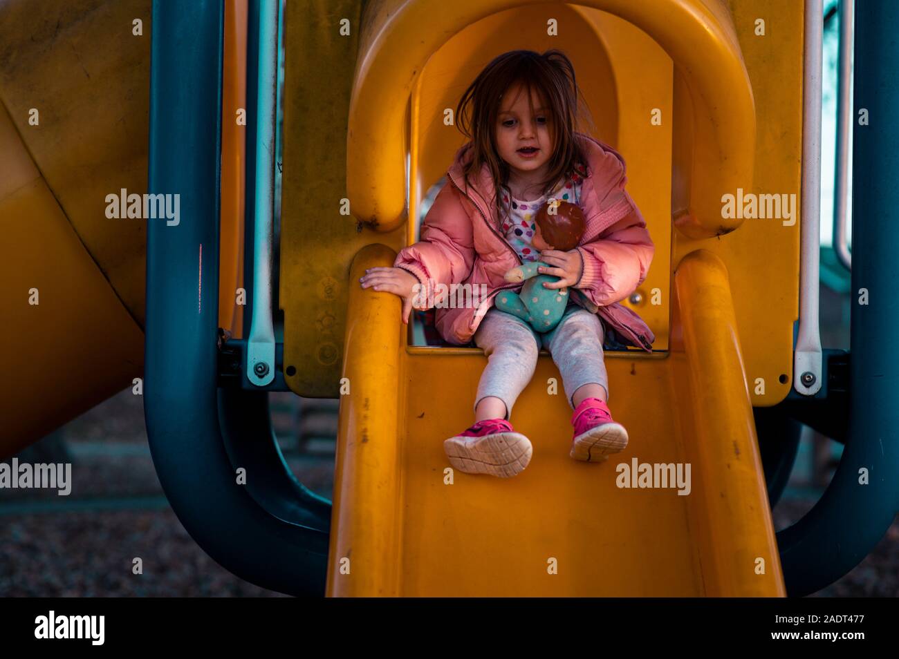 La ragazza si siede sulla diapositiva giallo in camicia rosa con vintage baby doll. Foto Stock