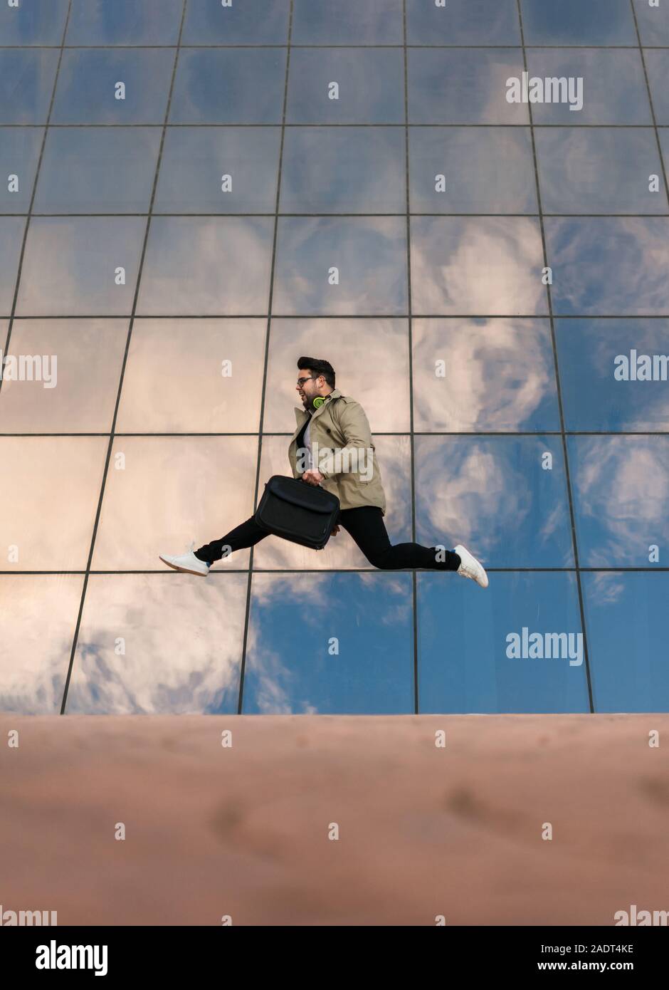 Imprenditore è jumping con un edificio vetrato nella parte posteriore Foto Stock
