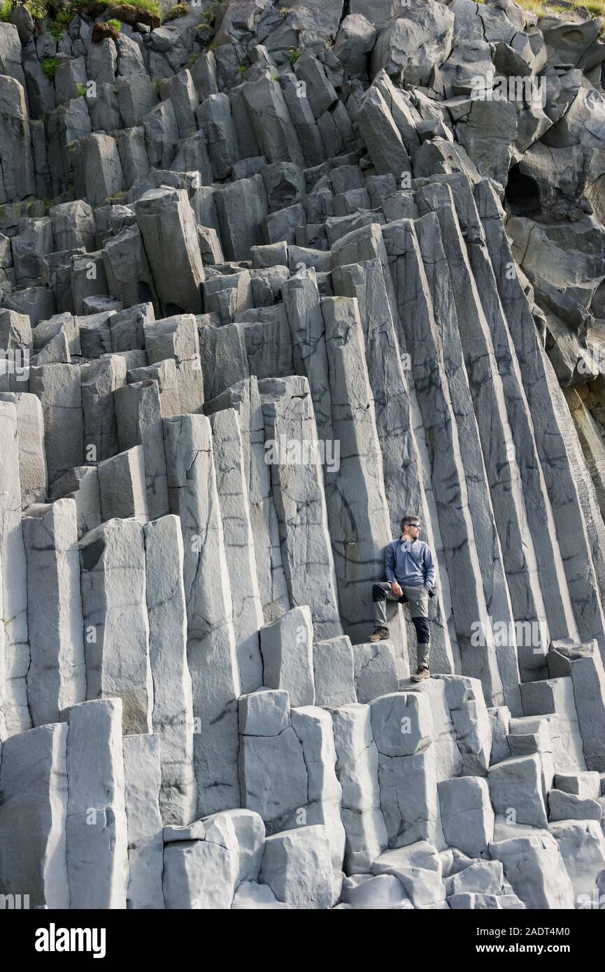 Uomo in posa di un gruppo verticale delle colonne di basalto sulla spiaggia di Vik, Islanda. Concetto di geologia Foto Stock