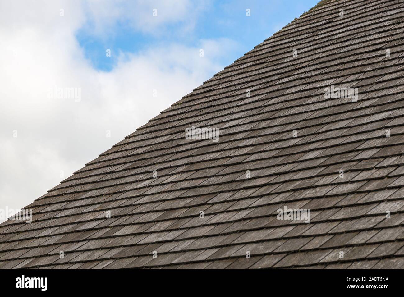 Tetto di ardesia grigia di piastrelle con un nuvoloso cielo blu sullo sfondo Foto Stock