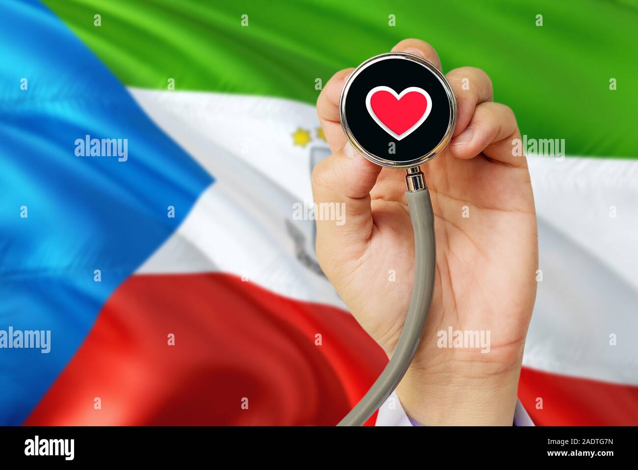 Medico tenendo uno stetoscopio con rosso cuore d'amore. Nazionale di Guinea Equatoriale bandiera dello sfondo. Assistenza sanitaria il concetto di sistema, tema medico. Foto Stock