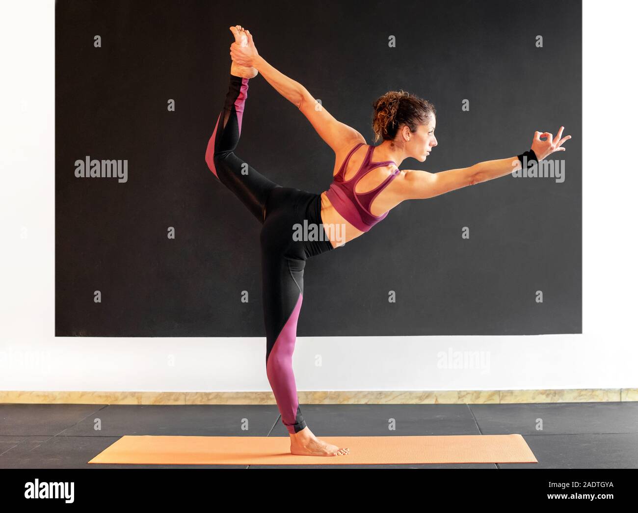 Giovane donna di eseguire un Natarajasana Yoga asana o signore della danza pongono, in equilibrio su una gamba braccio proteso in una palestra in una vista di profilo in una guarire Foto Stock
