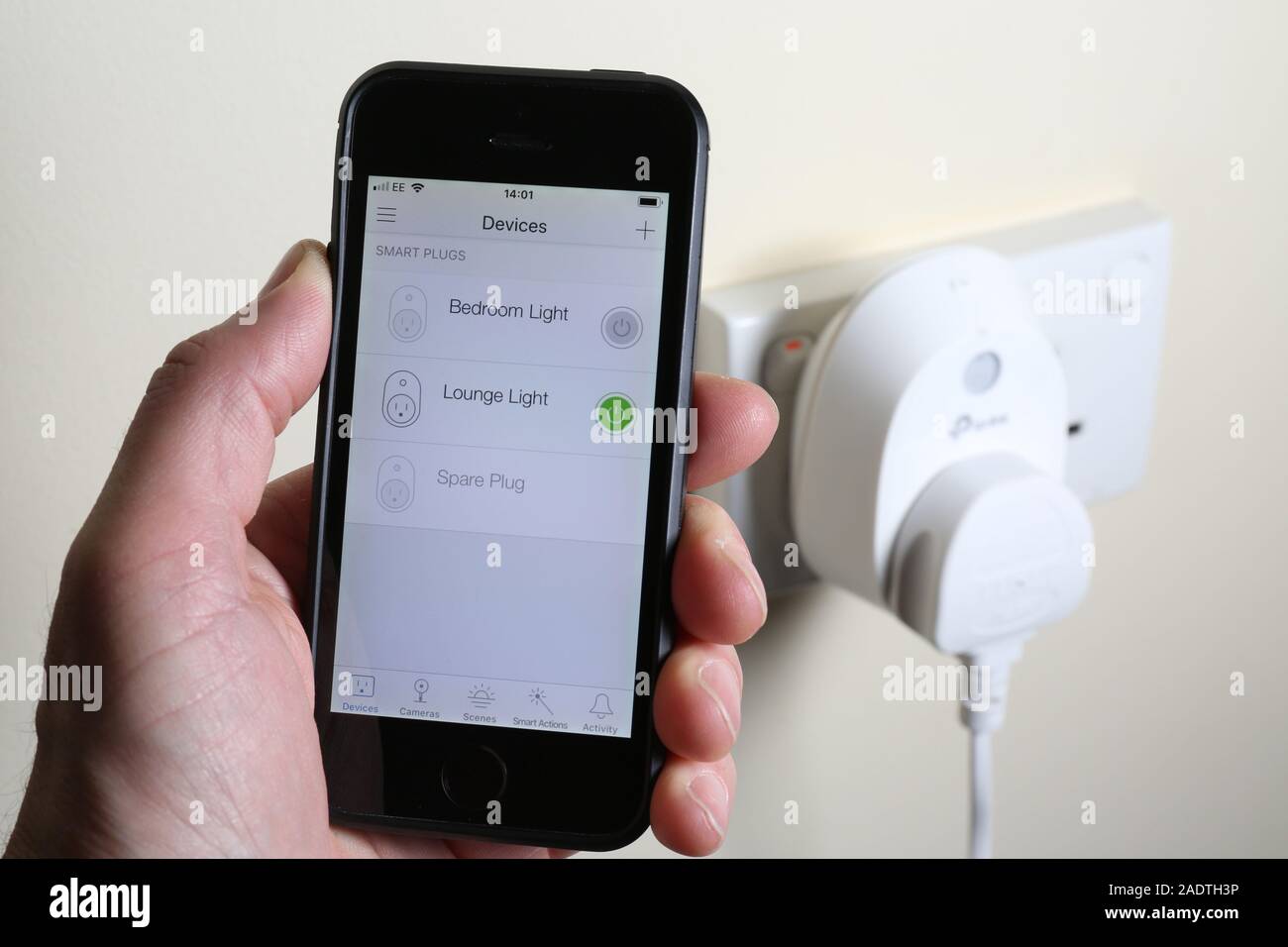 Un uomo di accendere una luce tramite una smart plug con un'app sul suo telefono cellulare. Foto Stock