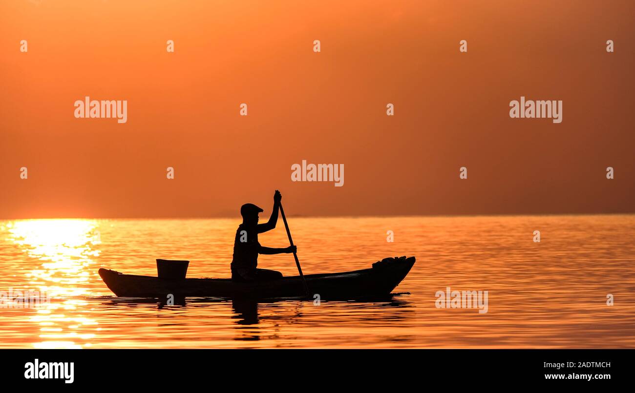 Un pescatore paddling durante il tramonto disegna una silhouette perfetta nel Lago Malawi Foto Stock