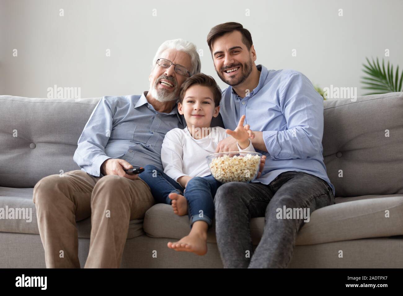 Allegro nonno cresciuto, figlio e nipote di guardare la TV mangiare popcorn Foto Stock