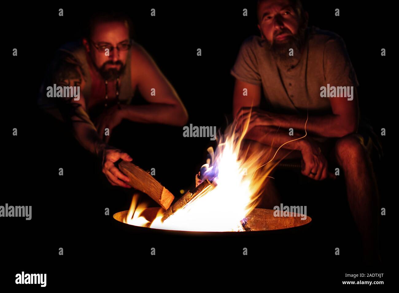 Due uomini seduti su un fuoco, il fuoco su un focolare di notte, vita all'aria aperta con gli amici Foto Stock