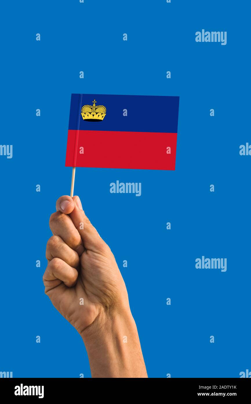 Donna mano azienda Liechtenstein bandiera con bastone, sventola bandiera sul profondo blu del cielo. Tema nazionale, profondo cielo blu. Foto Stock