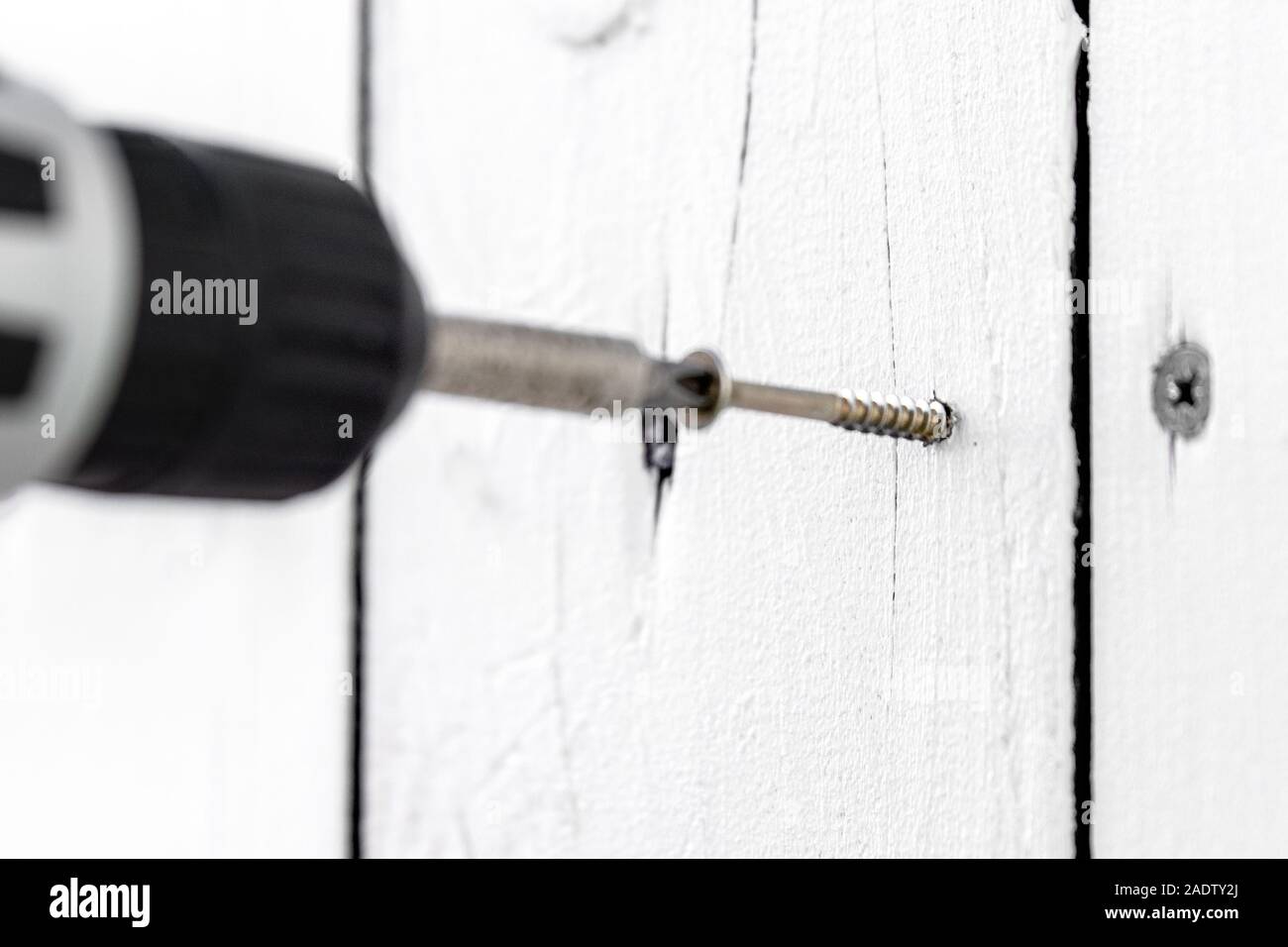 Un pannello truciolare vite viene avvitata in un bordo, tavola di legno è fissato con la vite con un cacciavite a batteria Foto Stock