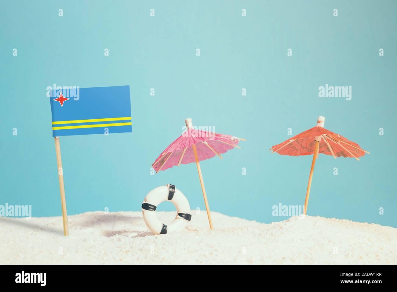 Bandiera in miniatura di Aruba sulla spiaggia con ombrelloni colorati e salvagente. Concetto di viaggio, Tema estivo. Foto Stock