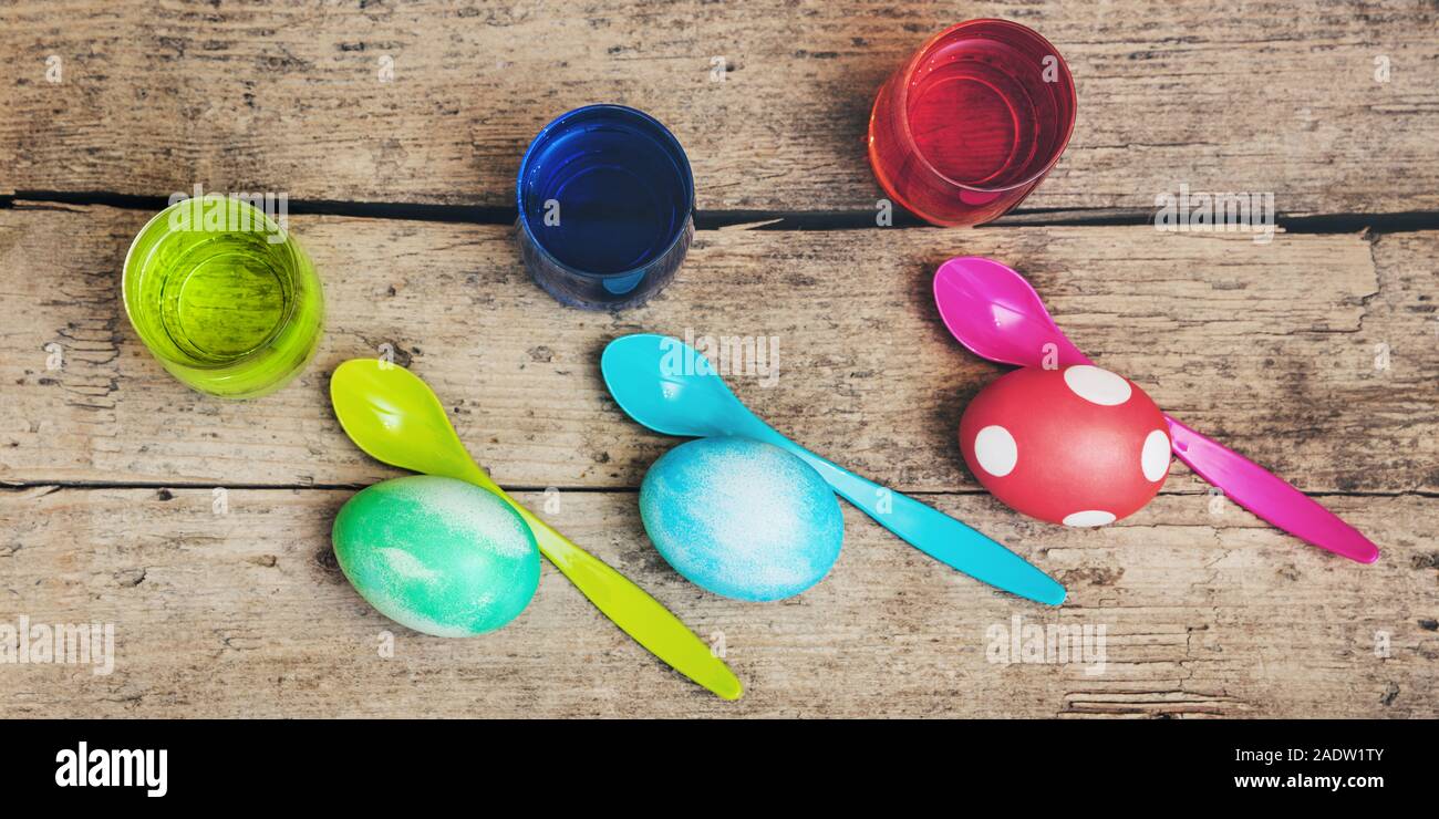 Flatlay, colorate uova di pasqua, coloranti di uovo e cucchiai sul tavolo di legno, testata Foto Stock