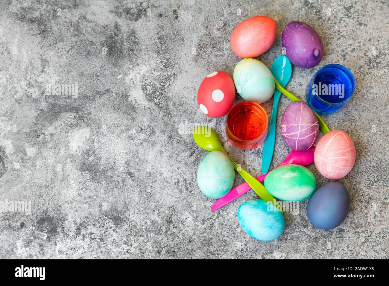 Flatlay, tinte colorate uova di pasqua, cucchiai e coloranti di uovo su sfondo grigio, biglietto di auguri con copyspace Foto Stock