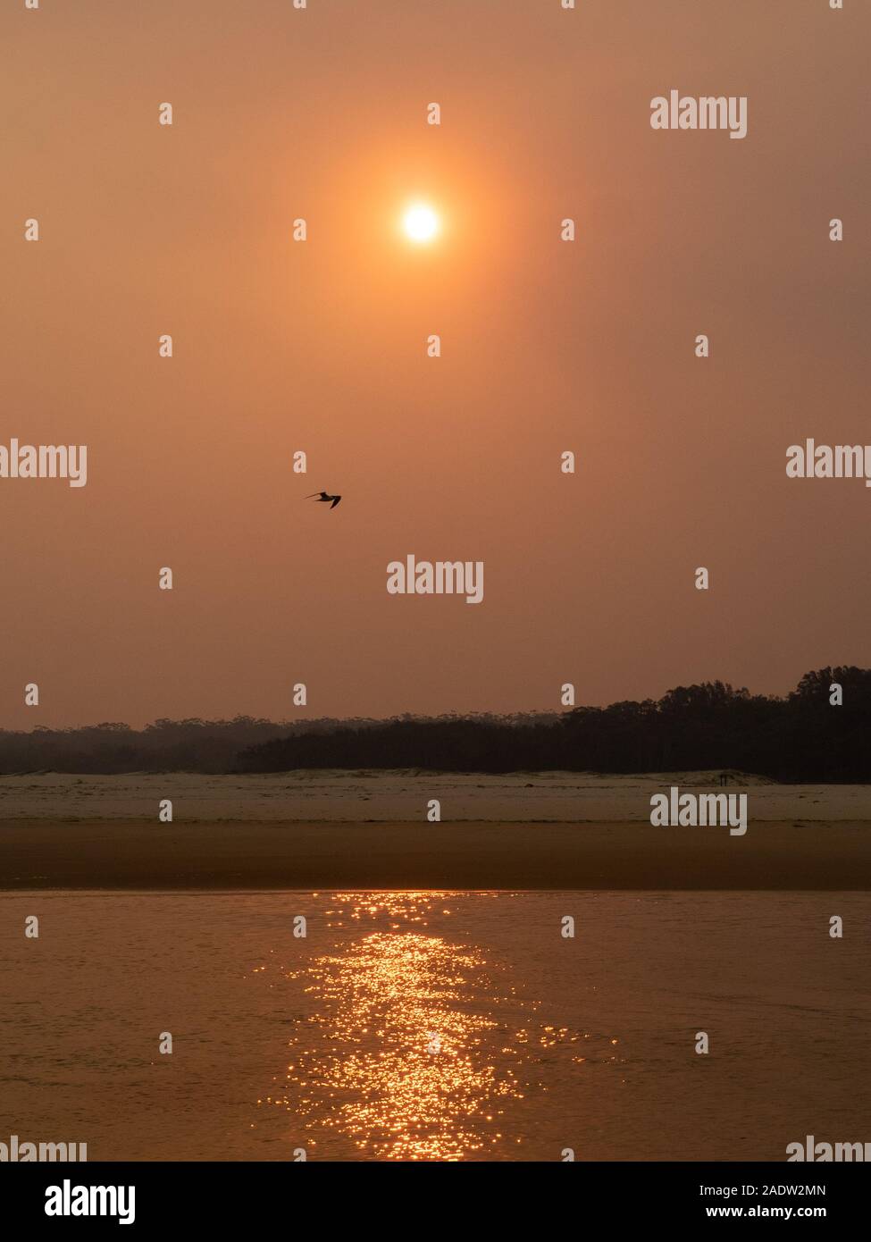 Smokey arancione sun riflessa nell'oceano sopra la spiaggia Foto Stock