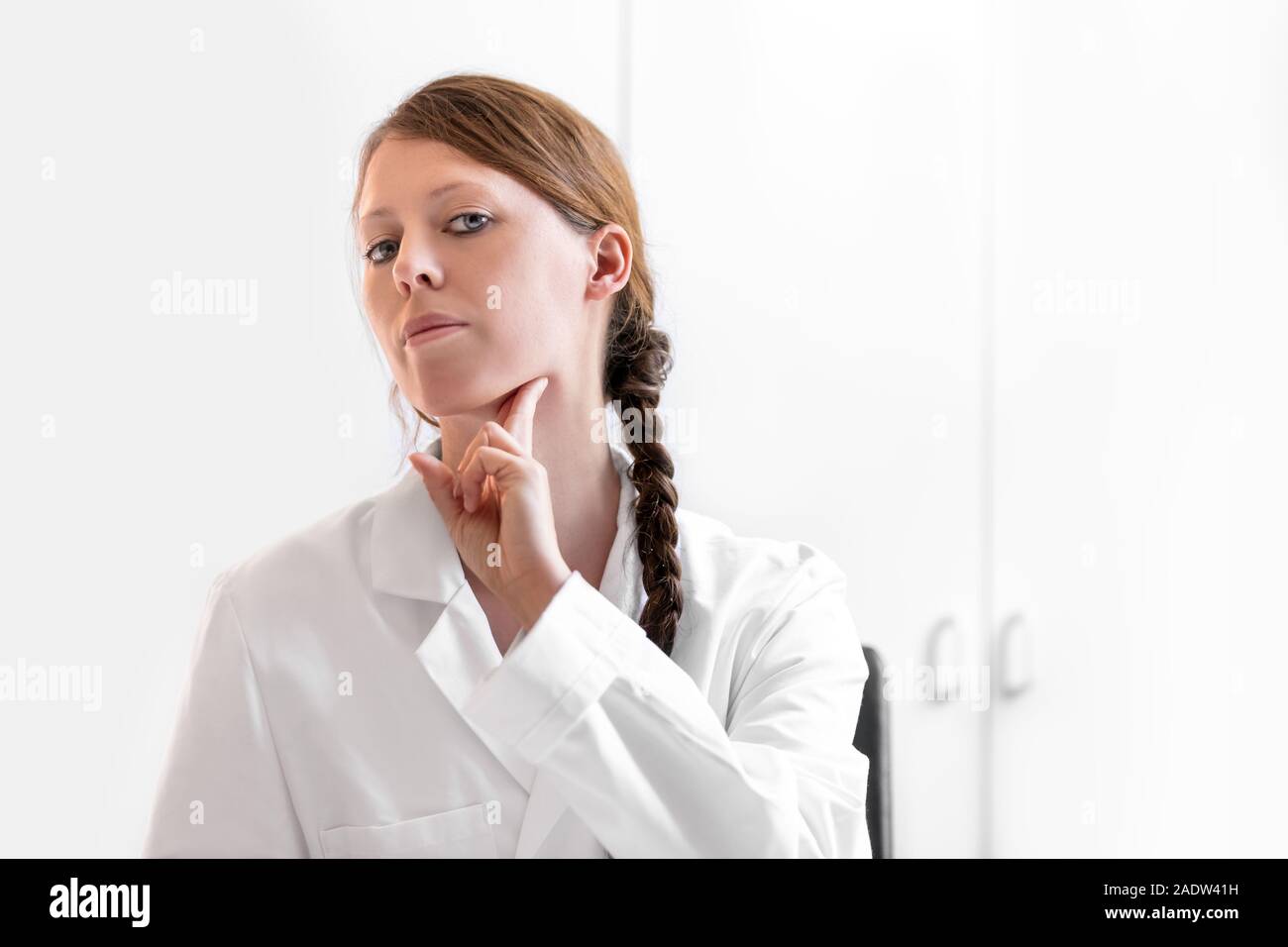 Giovani donne medico che mostra come verificare e controllare un nodo linfatico, sfondo bianco con copyspace Foto Stock