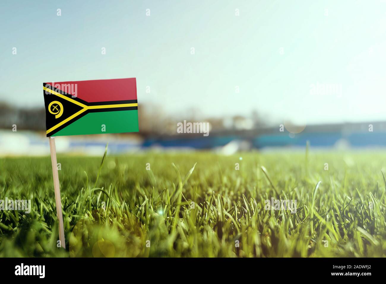 Stick miniaturizzato Vanuatu bandiera su erba verde, vicino campo di sole. Lo sfondo dello stadio, copia spazio per il testo. Foto Stock