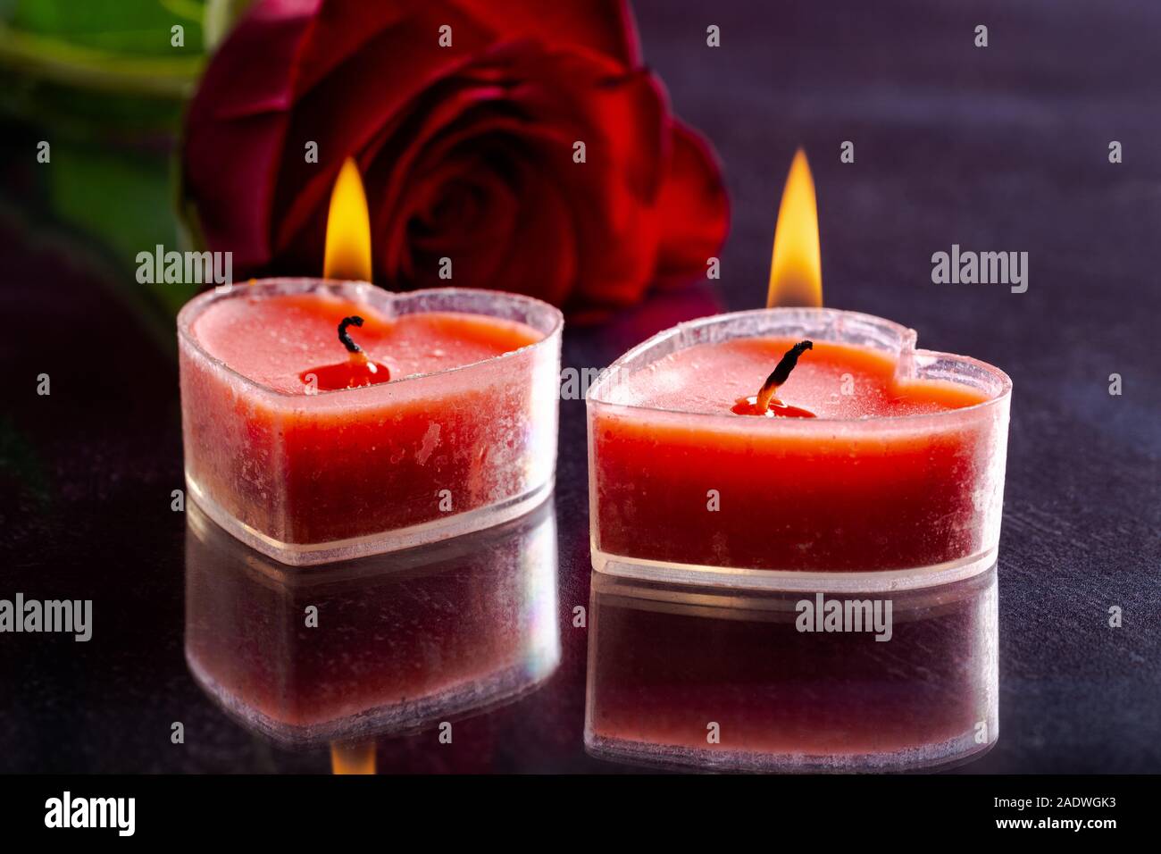 Primo piano di due cuore ardente di san Valentino a forma di candele con una rosa rossa in background su un tavolo scuro Foto Stock