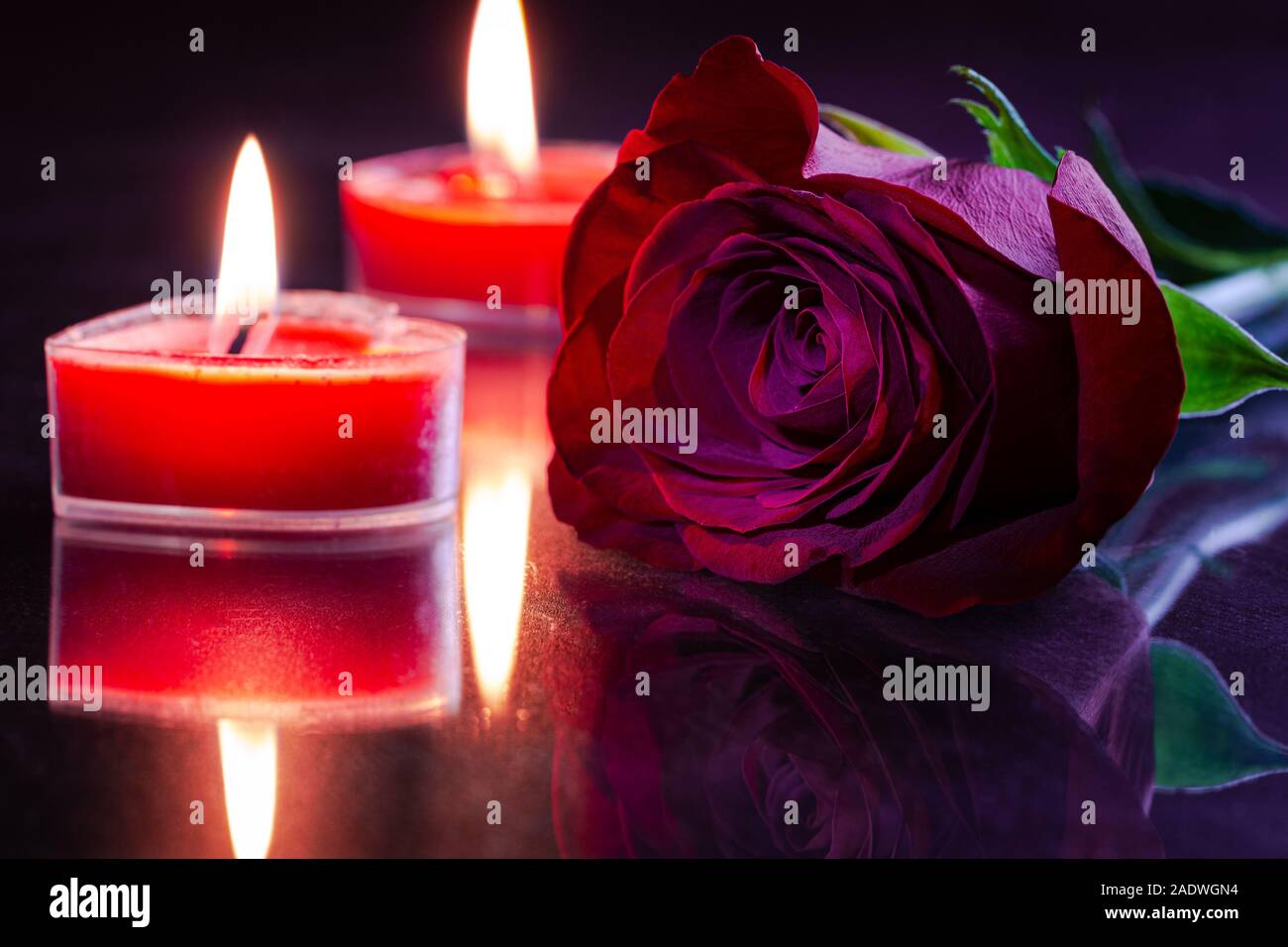 Primo piano di una rosa rossa con due burning valentine candele su una riflettente tabella scuro Foto Stock