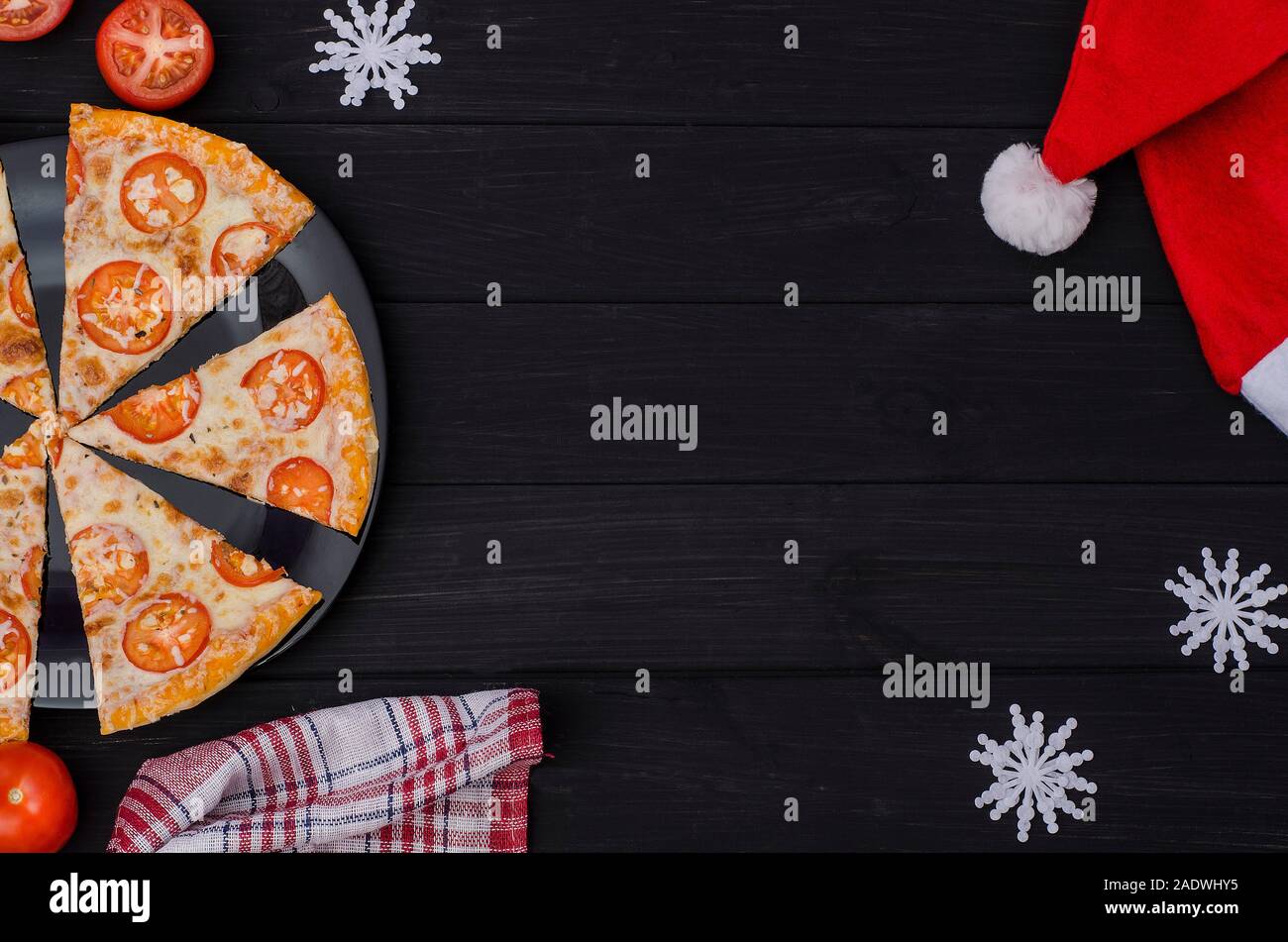 Ordinare una pizza per le vacanze: Capodanno e Natale. Pezzi di pizza con il formaggio e i pomodori su una piastra nera con ingredienti su un backgro nero Foto Stock