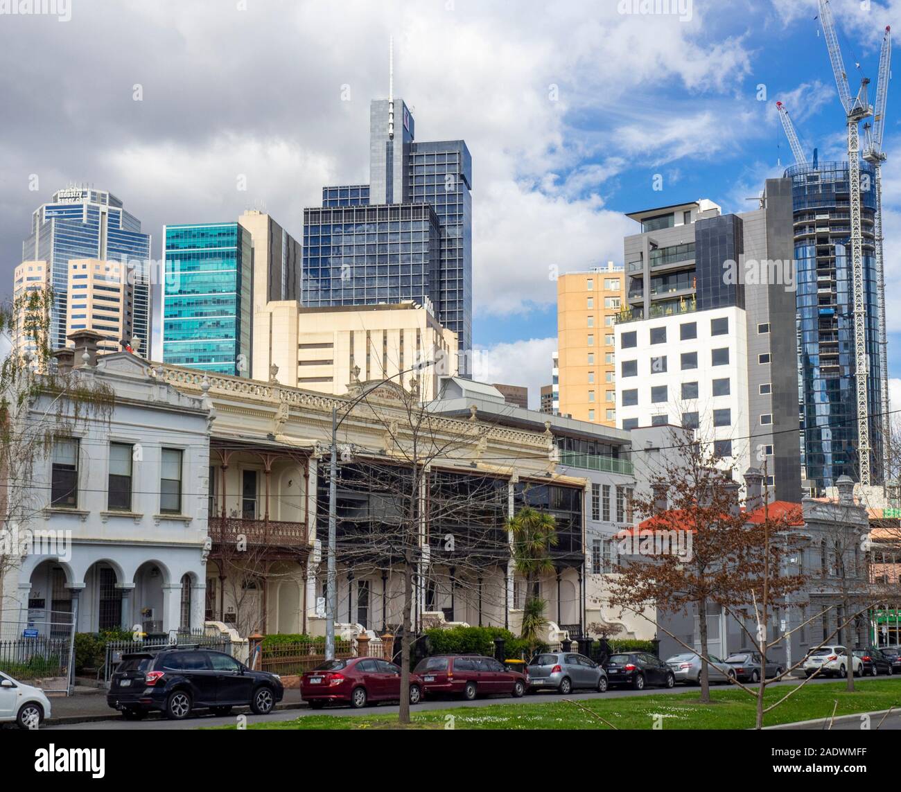 Veicoli parcheggiati davanti a una fila di case terrazza su Drummond St Carlton e il CBD ufficio torri e grattacieli in background Melbourne Australia. Foto Stock