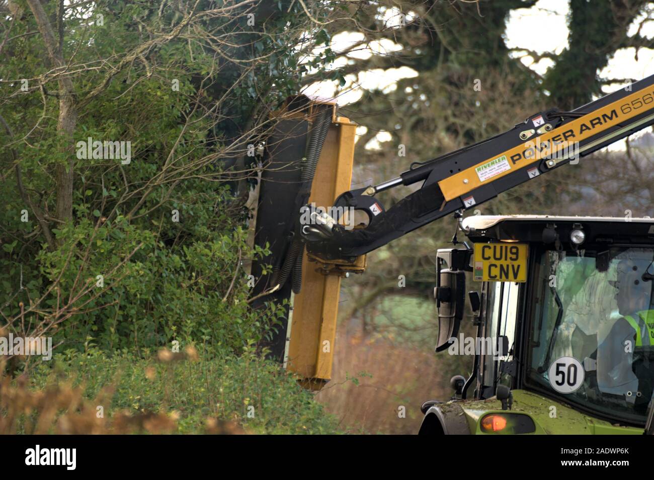 Aberystwyth Ceredigion nel Galles/UK Dicembre 04 2019: Giallo trattore taglio di siepi su un paese rurale lane Foto Stock